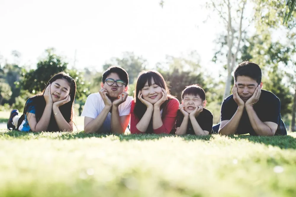 Uma família de cinco pessoas, deitada no gramado e sorrindo alegremente, durante sua estadia no Japão.