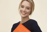 A foreign woman smiles at us while holding a Japanese textbook.